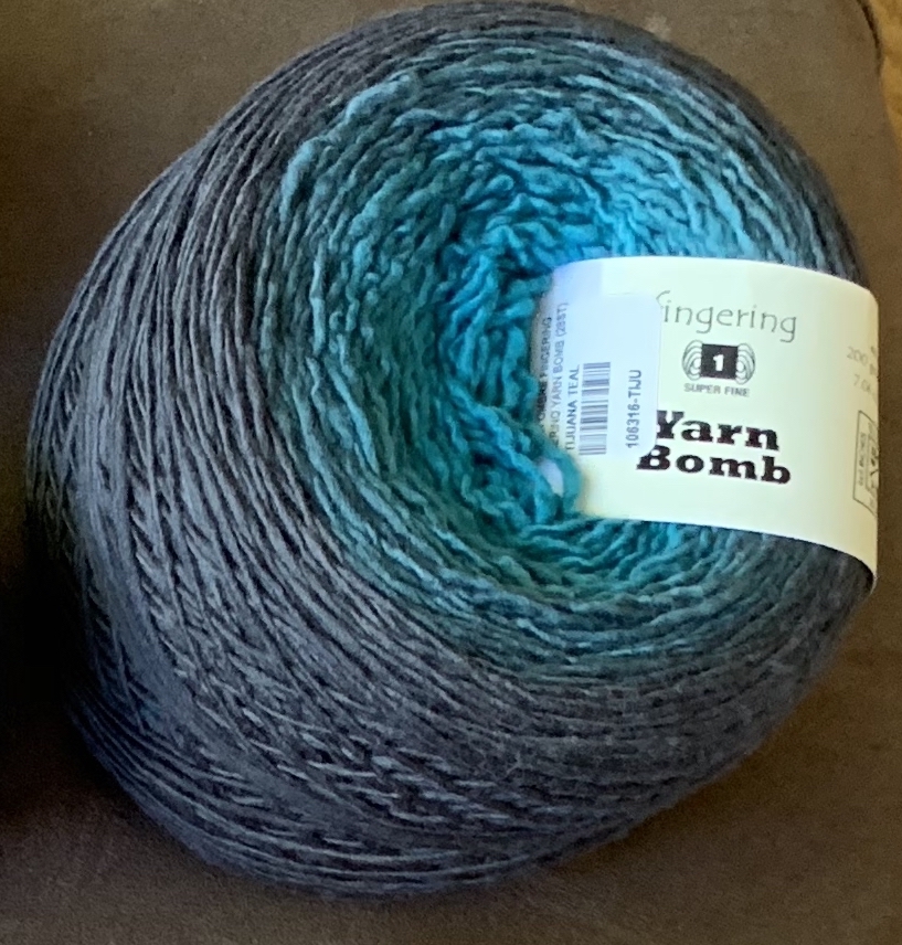 A teal to gray ombre cake of fingerling-weight yarn labeled YarnBomb.